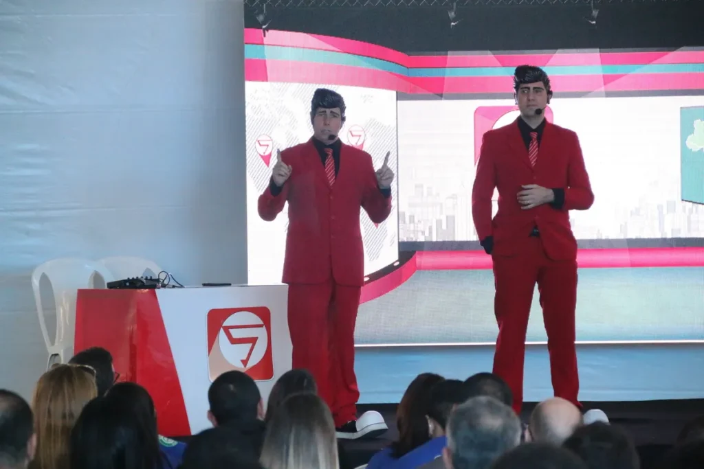 Dois palestrantes vestidos de terno vermelho apresentam-se em um evento diante de um público, em palestra sobre apneia do sono e saúde respiratória.