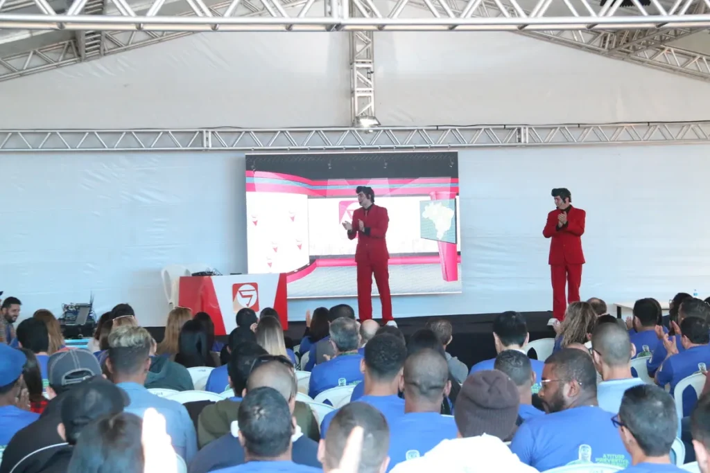 Dois palestrantes de terno vermelho falam em palco diante de um público, durante apresentação sobre apneia do sono e conscientização em saúde.