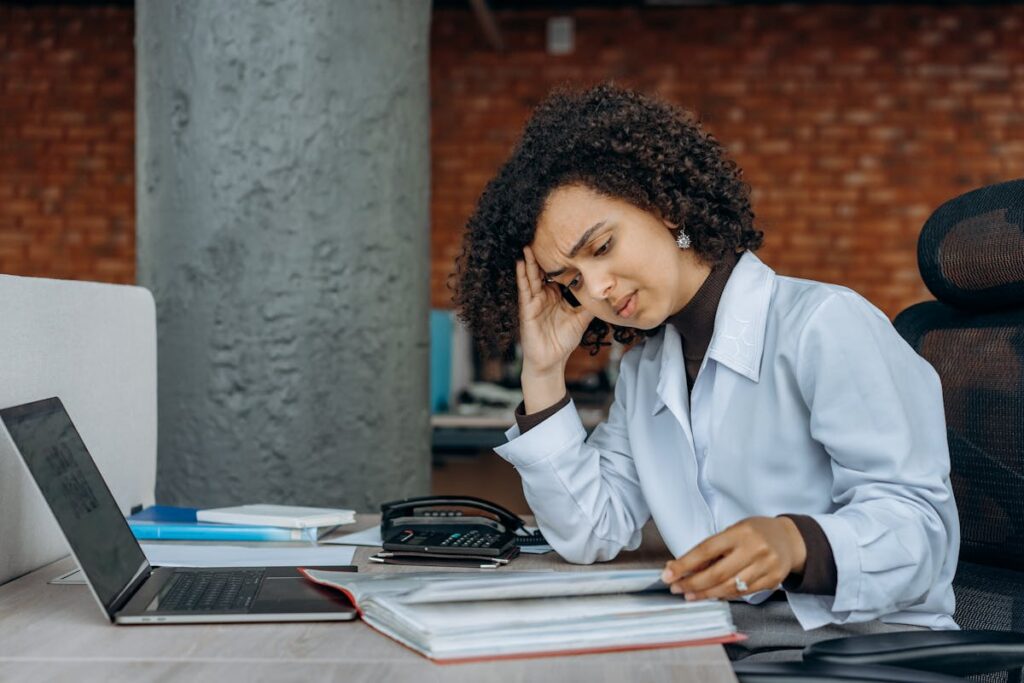 Mulher de frente para o computador, com a mão na cabeça, parecendo cansada