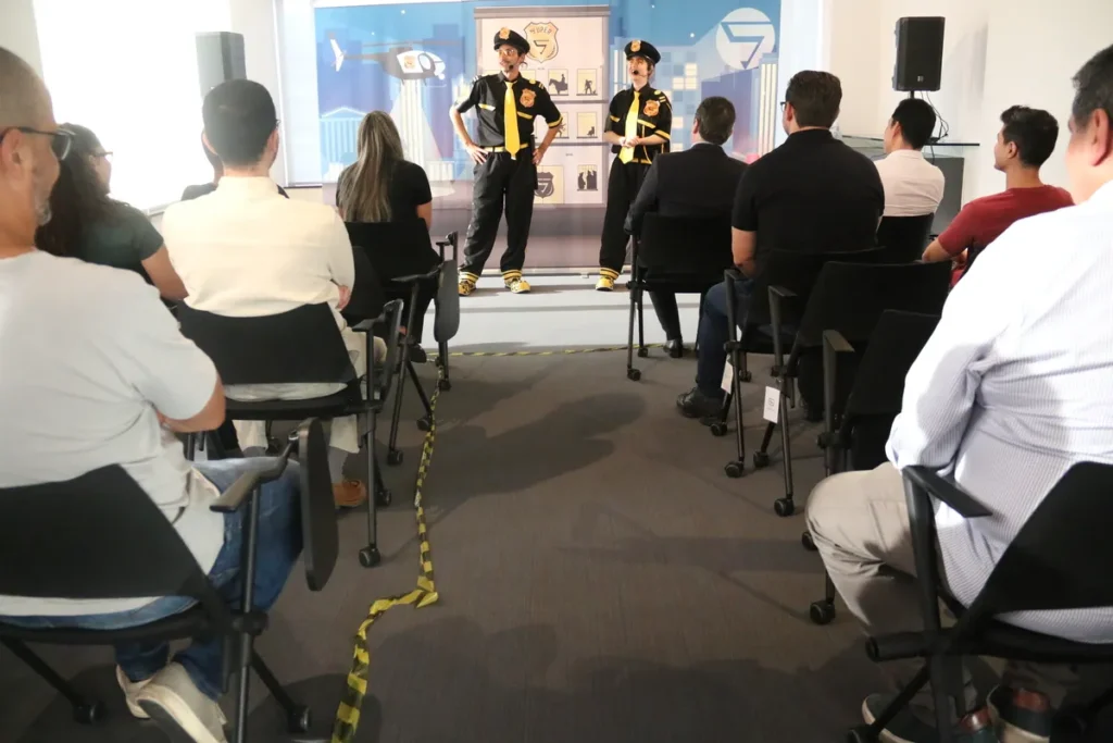 Dois homens, vestidos com uniformes de segurança, fazendo uma apresentação sobre calçados de segurança para uma plateia.