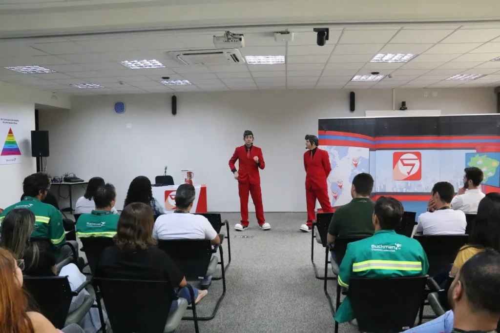 Palestrantes em trajes vermelhos em um palco, dirigindo-se a uma plateia em uma palestra sobre conscientização e saúde.