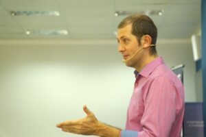 Palestrante usando microfone headset e camisa rosa durante apresentação corporativa de SIPAT.