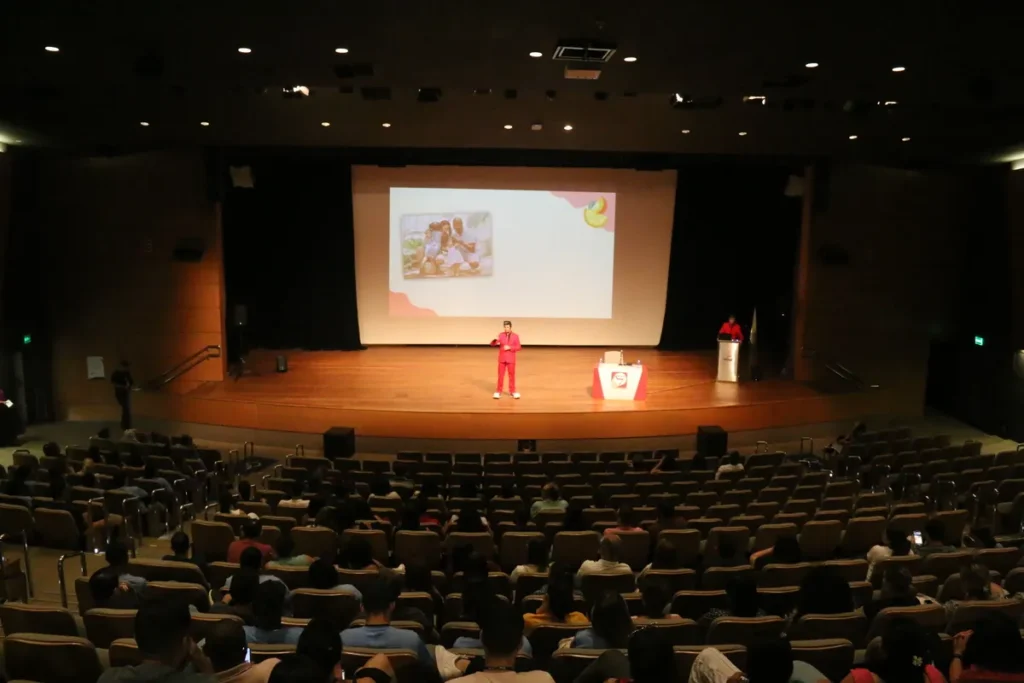 Palestra em um grande auditório sobre nutrição, com um slide na tela que menciona o tema "gordura" e suas variações.