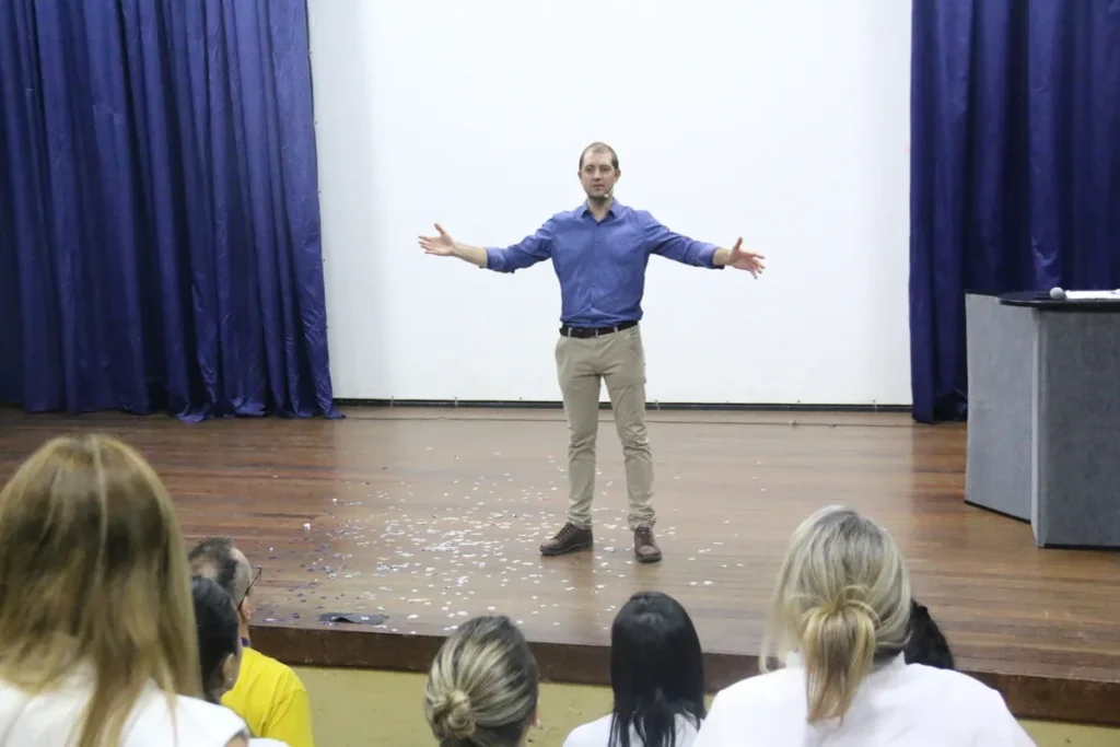 Homem de pé em um palco, com os braços abertos, em frente a uma plateia, em uma palestra de coaching motivacional.Coaching motivacional: a importância de inspirar e guiar pessoas em busca de seus objetivos