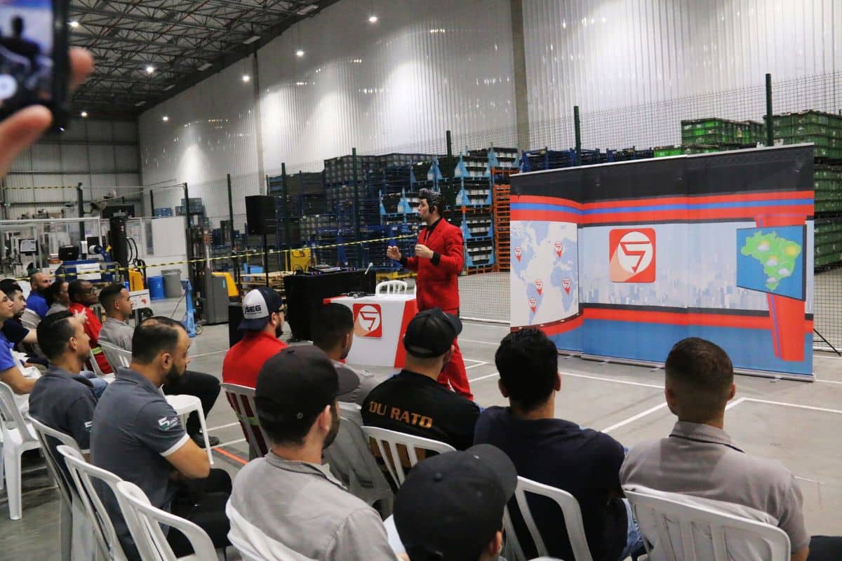 Instrutor realiza palestra sobre cultura de segurança do trabalho para colaboradores em galpão industrial.