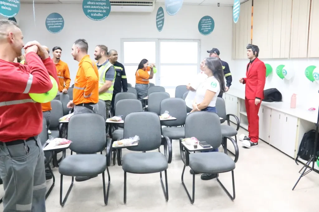 Palestrante em terno vermelho interagindo com funcionários em uma palestra sobre segurança do trabalho e prevenção de doenças como a dermatite de contato.