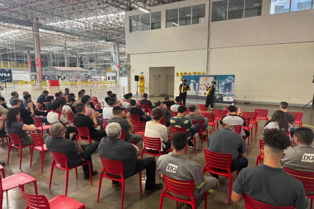 Palestrantes em um palco, falando para uma plateia de funcionários em um galpão industrial, em um evento de conscientização contra o desmatamento.