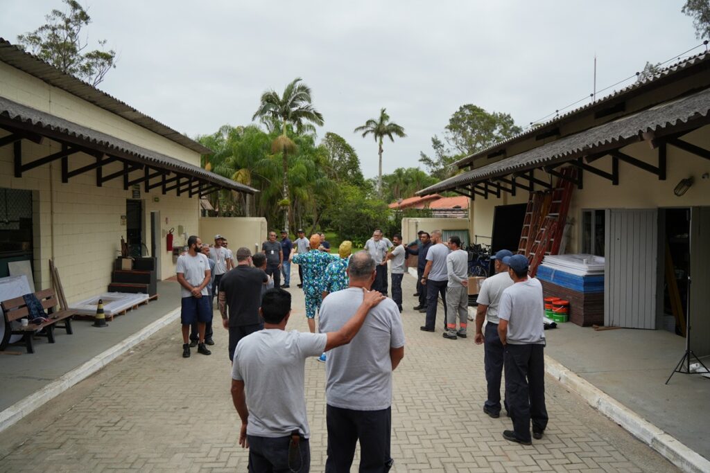 Grupo de colaboradores reunidos em dinâmica de integração ao ar livre durante atividade corporativa voltada ao equilíbrio emocional e trabalho em equipe