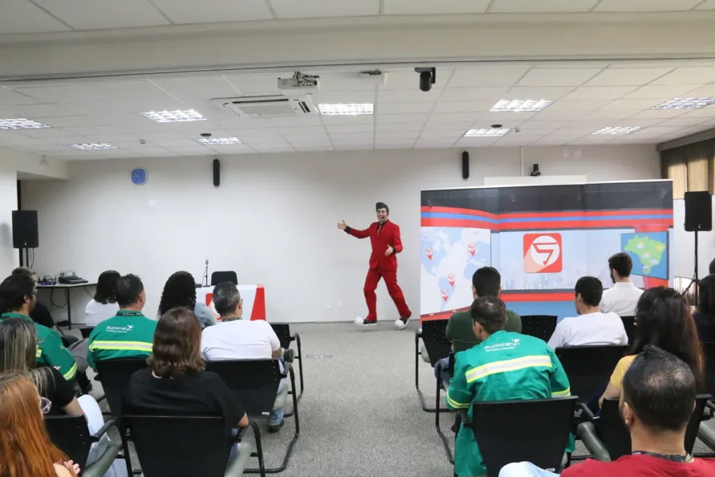 Um palestrante com um terno vermelho gesticulando energicamente para uma plateia em um auditório, durante uma palestra sobre exaustão mental e bem-estar no trabalho.