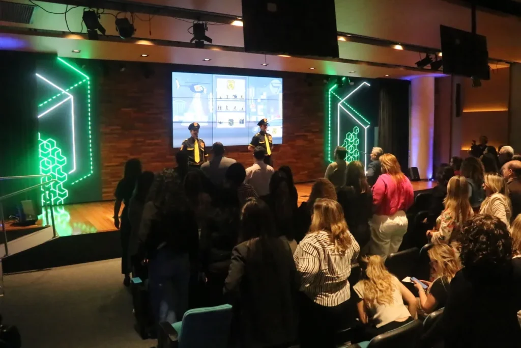 Público atento a palestrantes em evento com possível uso de frases motivacionais engraçadas.