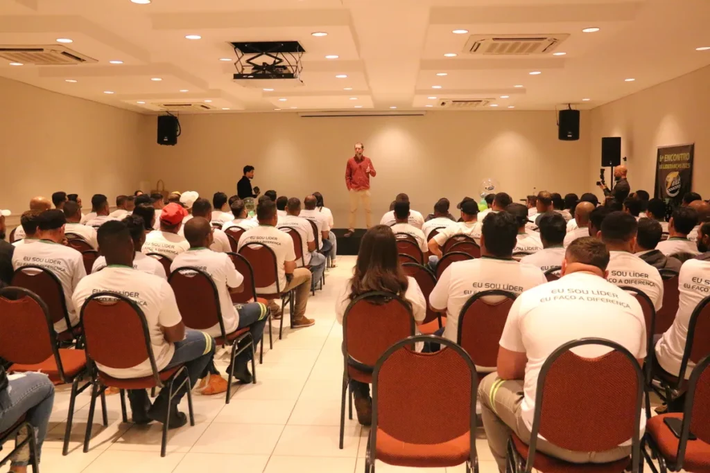 Palestrante em camisa vermelha apresentando para uma plateia com camisetas "Eu Sou Líder, Eu Faço a Diferença" em um seminário, relevante para conscientização sobre HPV.