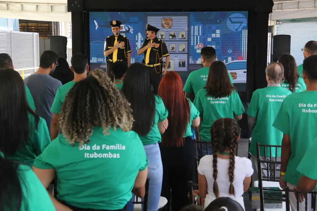 inflamação joelho, dois homens em uniformes de segurança em um palco, com um público usando camisetas verdes e assistindo a um evento.