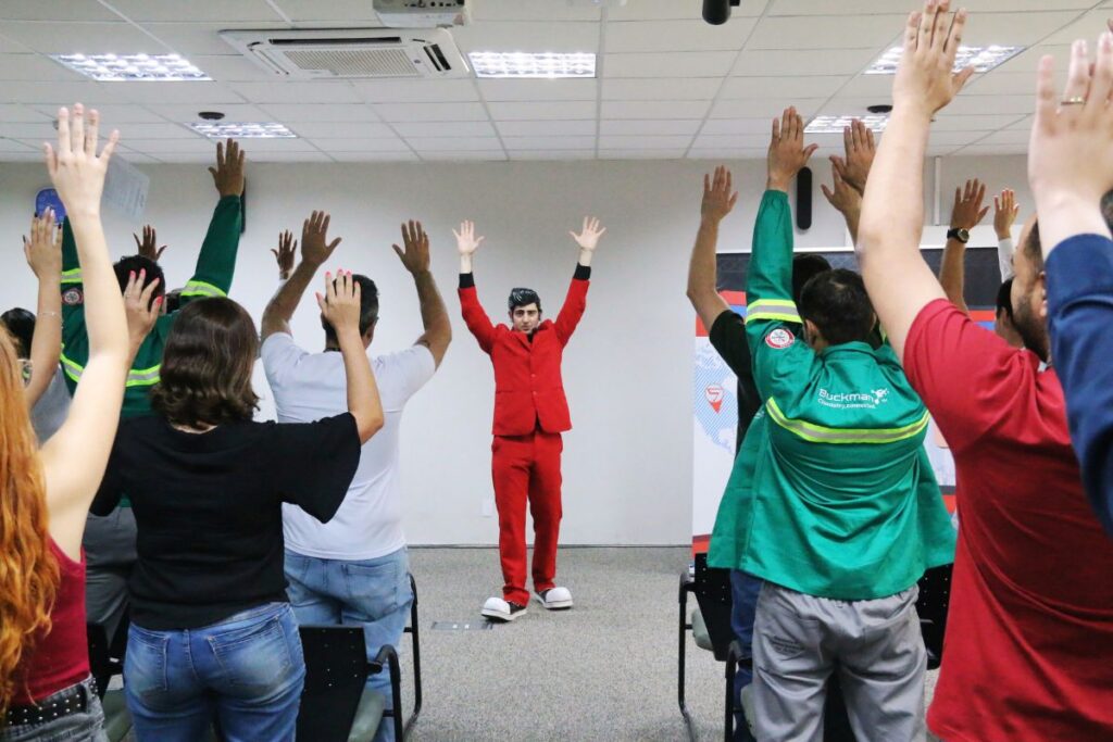 Colaboradores participam de dinâmica interativa com instrutor durante treinamento de cultura de segurança do trabalho em sala corporativa.