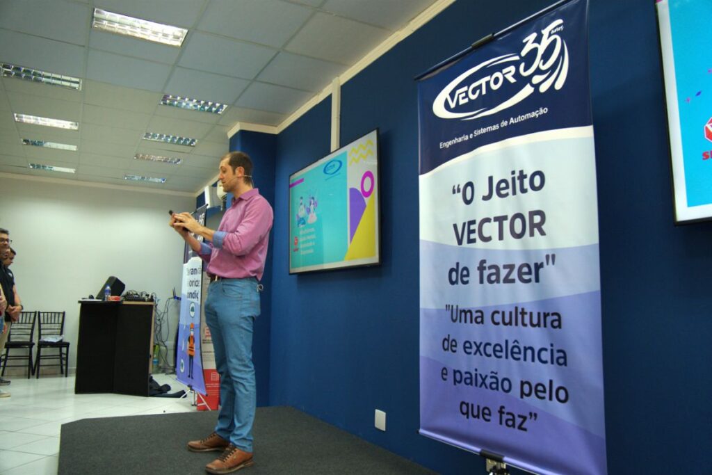 Palestrante em palco corporativo falando com microfone durante apresentação para equipe em evento de SIPAT.