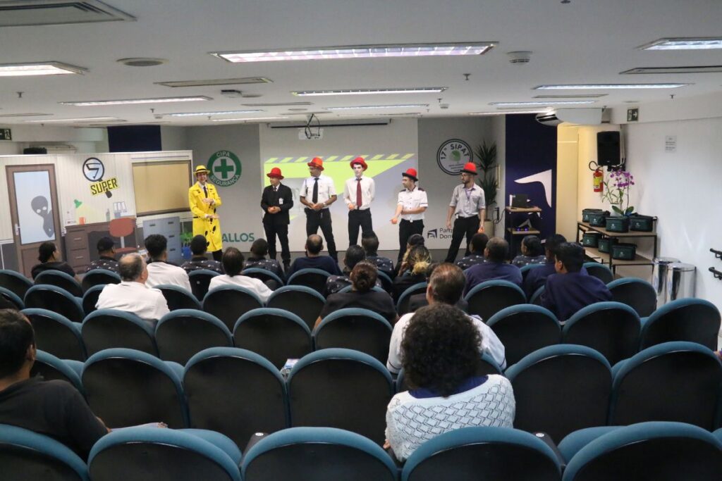 Funcionários assistindo apresentação teatral de segurança do trabalho durante treinamento SIPA em auditório corporativo