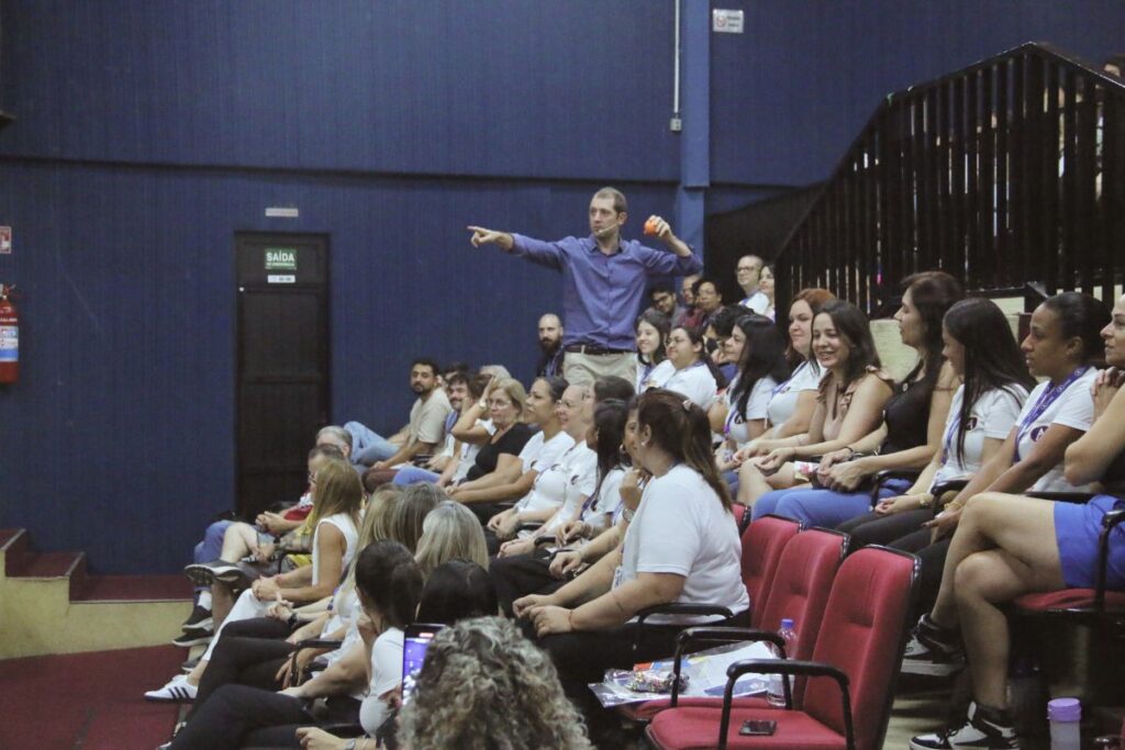 Palestrante interagindo com colaboradores sentados em auditório durante gravação de palestra para SIPAT online.