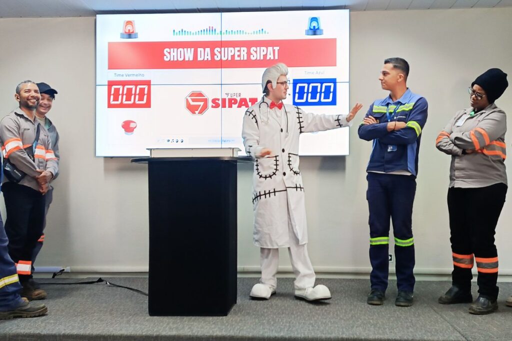 Apresentador caracterizado interagindo com colaboradores em apresentação chamada Show da Super SIPAT.