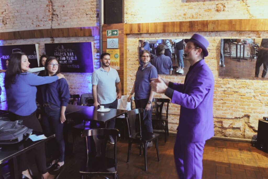 Palestrante com roupa roxa conduzindo atividade interativa com participantes durante palestra ao vivo para SIPAT online.