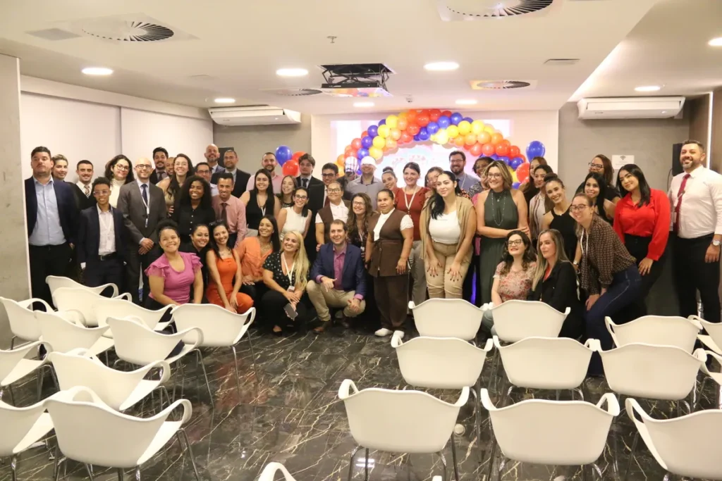 Grupo de pessoas em um evento, posando para uma foto em frente a um arco de balões, após participar de uma palestra sobre linfoma.