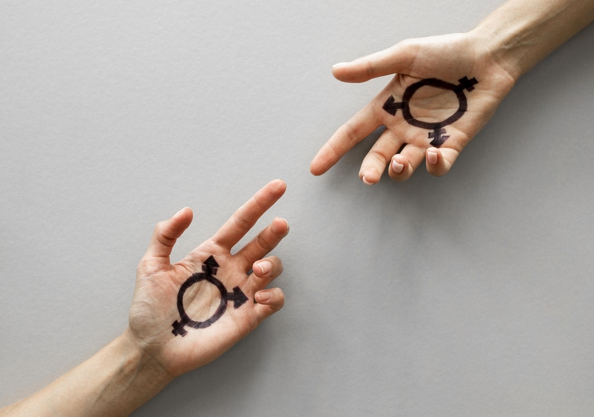 Duas mãos abertas com o símbolo transgênero desenhado nas palmas, sugerindo diversidade e expressão da identidade de gênero.