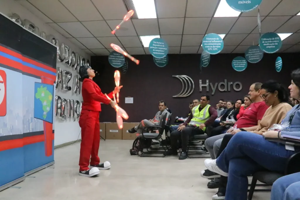 Palestrante malabarista de terno vermelho performa com claves luminosas em evento de segurança (NR-31) para colaboradores da empresa Hydro.