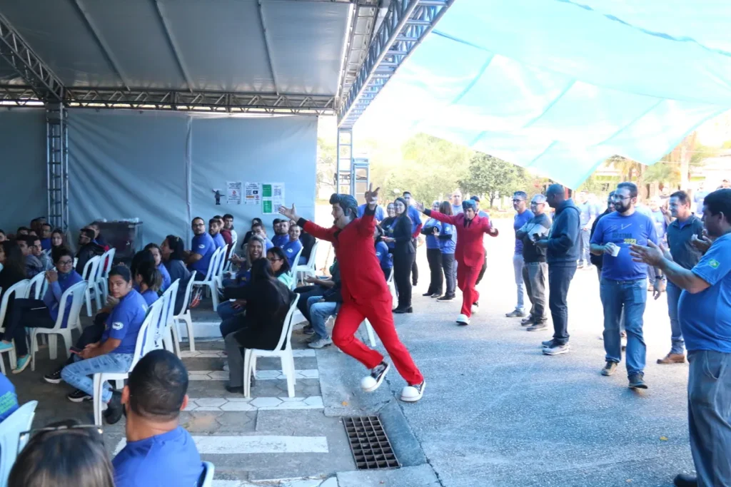 Colaboradores participam de dinâmica de grupo ao ar livre com instrutores vestidos de vermelho, utilizando um grande tecido azul.