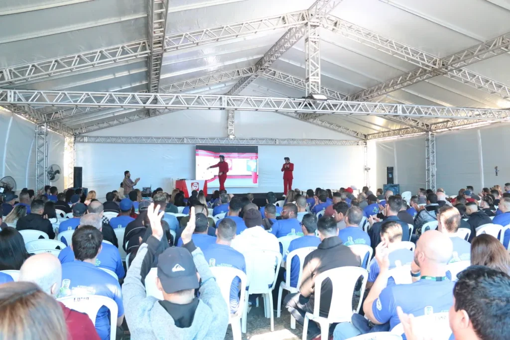 Uma palestra sobre nutrição e saúde em um grande evento, com dois palestrantes no palco e uma plateia engajada, muitos deles usando camisetas azuis.