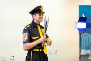 Palestrante vestido como agente de segurança, usando microfone headset e segurando objetos durante apresentação de SIPAT.