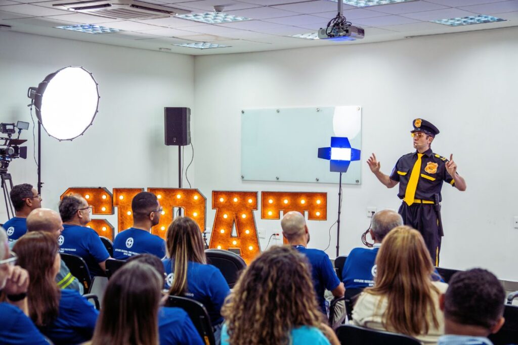 Instrutor ministrando treinamento de percepção de risco para equipe de segurança em sala corporativa equipada com iluminação profissional e painel iluminado.