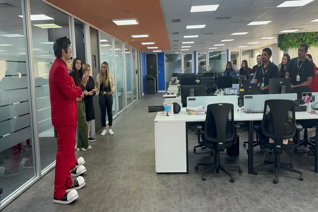 Facilitador em terno vermelho conduz dinâmica com colaboradores em um escritório, incentivando a proatividade