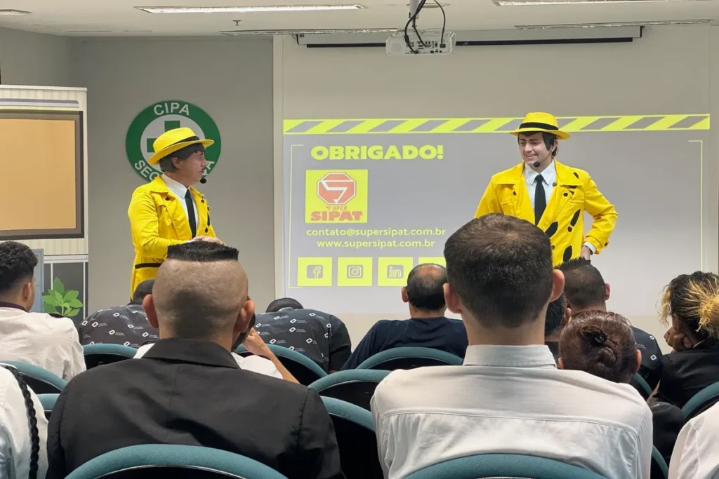 Dois homens vestidos com casacos e chapéus amarelos estão em um palco em frente a uma plateia. Eles parecem ser palestrantes em um evento sobre saúde e o logo do evento está visível ao fundo. A imagem representa o tema de protocolo de dor torácica.