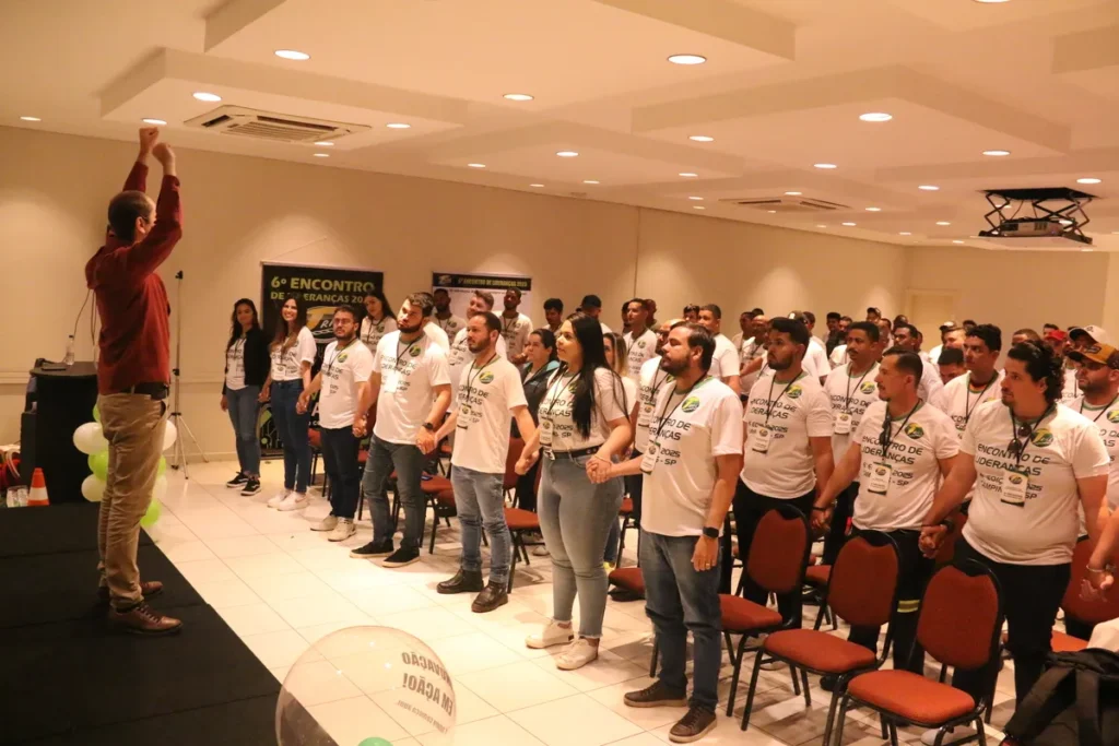 Público de mãos dadas em palestra, com palestrante no palco, em evento de conscientização