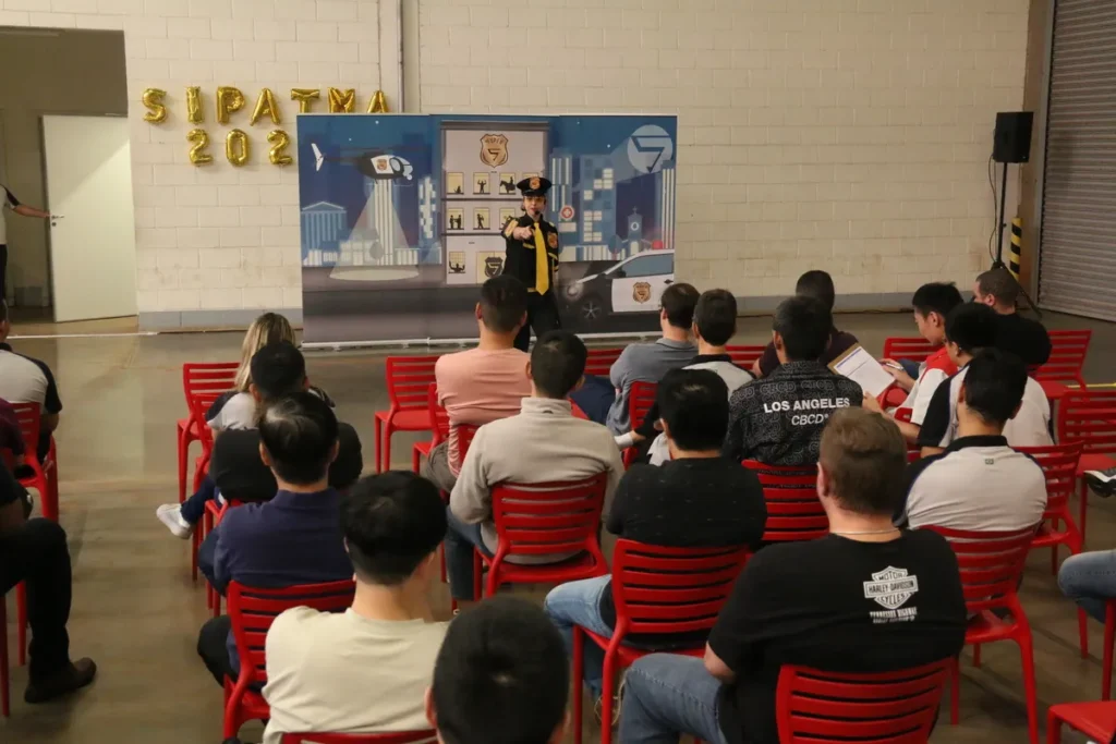 Pessoa fantasiada de policial, com detalhes amarelos, apresentando uma palestra sobre transtorno de personalidade para uma plateia em evento com a temática de segurança (SIPATMA 2021).