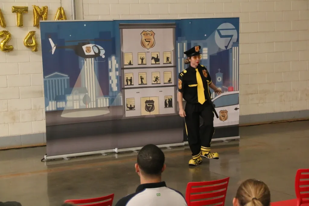 Pessoa fantasiada de policial, com detalhes amarelos, apresentando uma palestra sobre transtorno de personalidade em um evento, com painel temático de fundo.